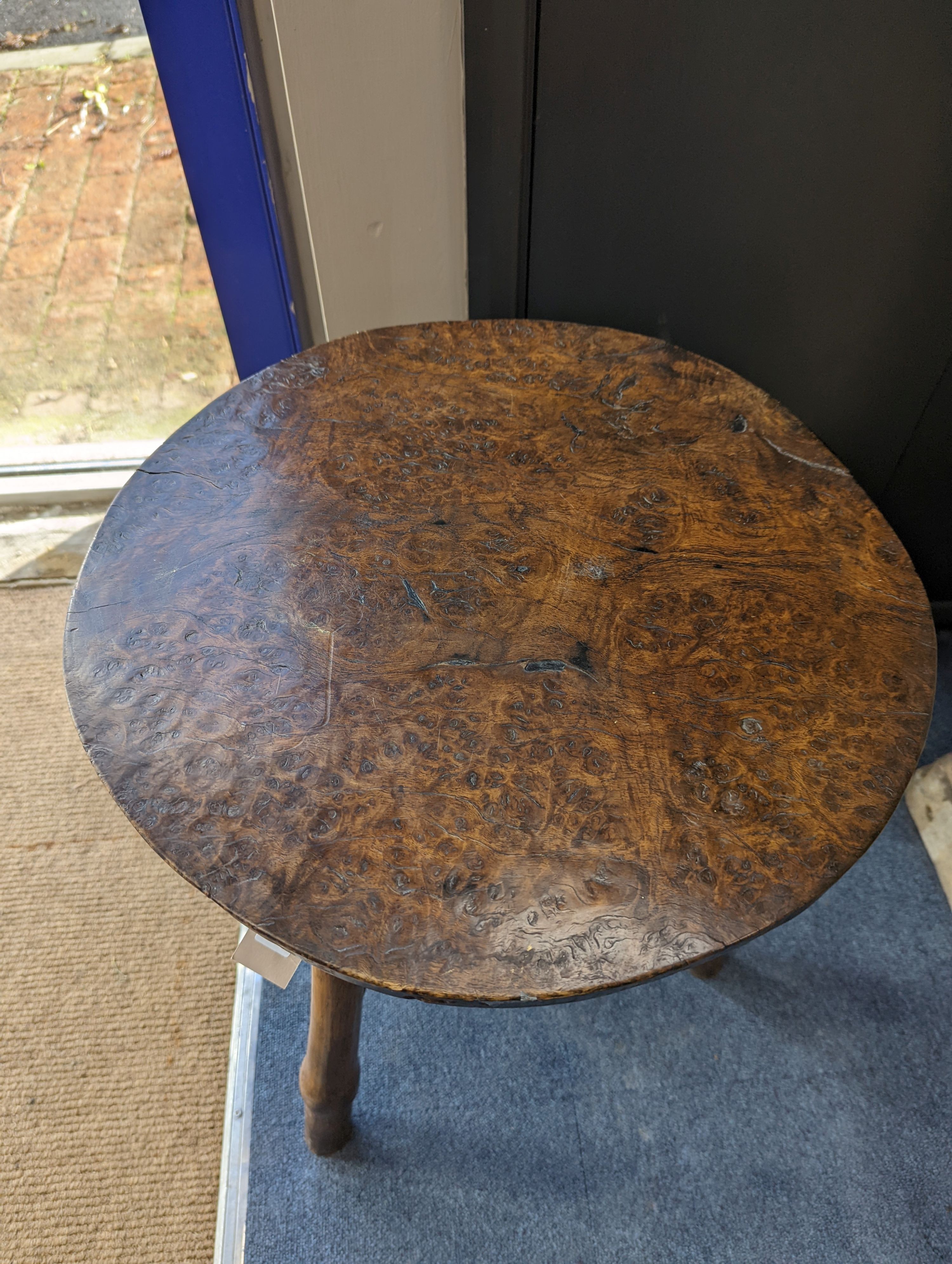 A circular burr elm and ash primitive cricket table with T shaped stretcher, diameter 44cm, height 61cm